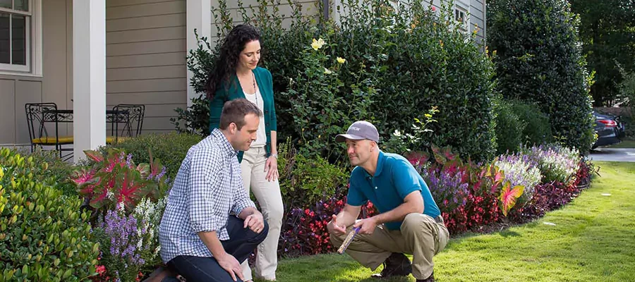 2 men sitting and one woman standing in front of the house garden and talking